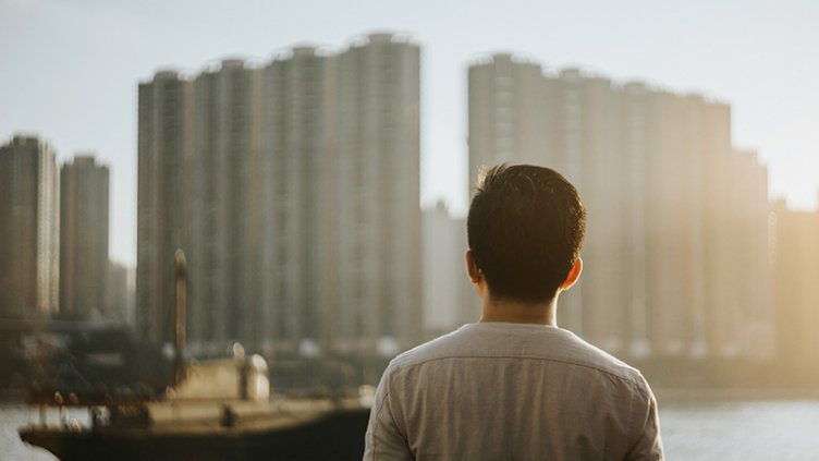 A man standing near the river and looking towards real estate building