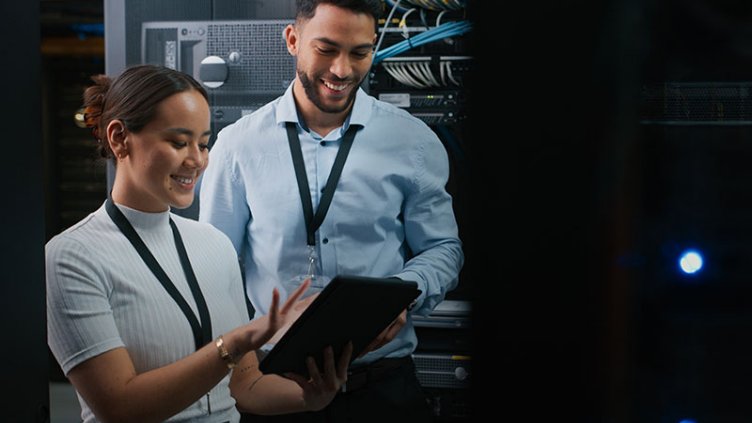 Two employees smiling while looking at the tablet inside data centre