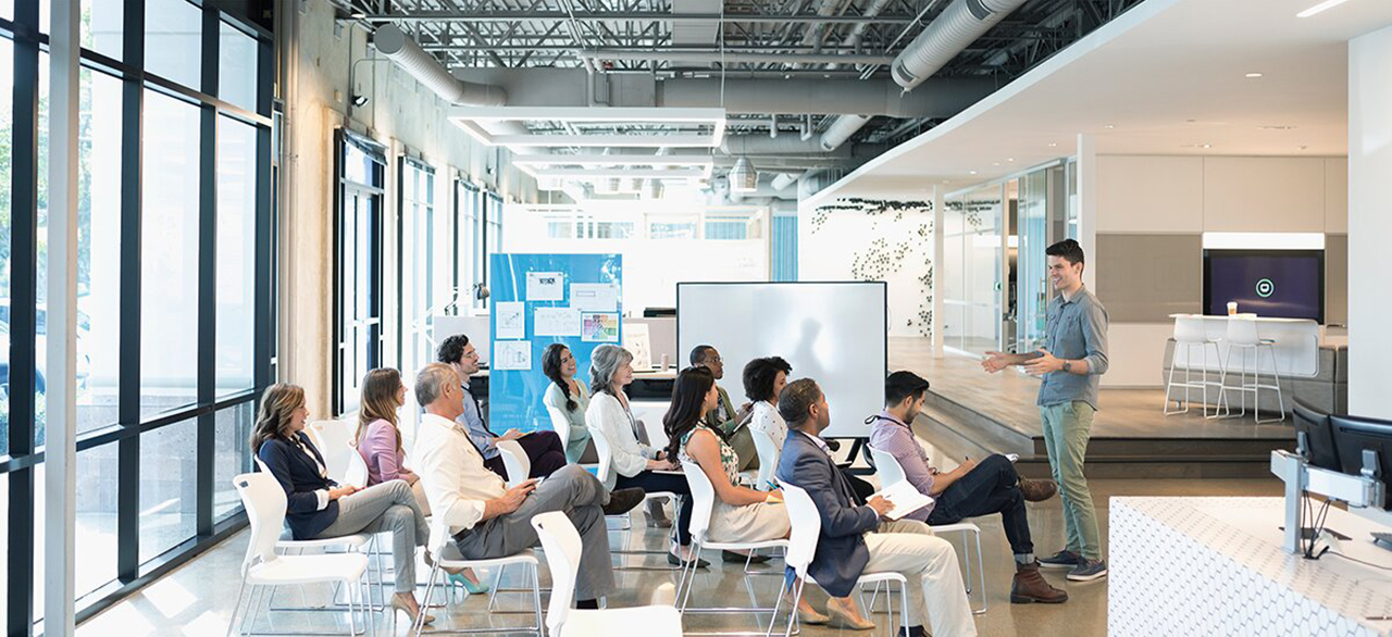 conference audience listening to businessman leading presentation in office